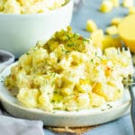 A serving of Easy Southern Potato Salad on a plate surrounded by chopped potatoes.