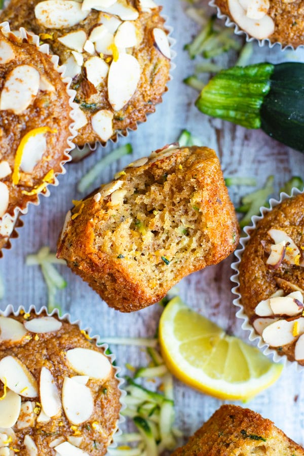 Gluten-free zucchini muffin with a bite inside surrounded by other muffins.