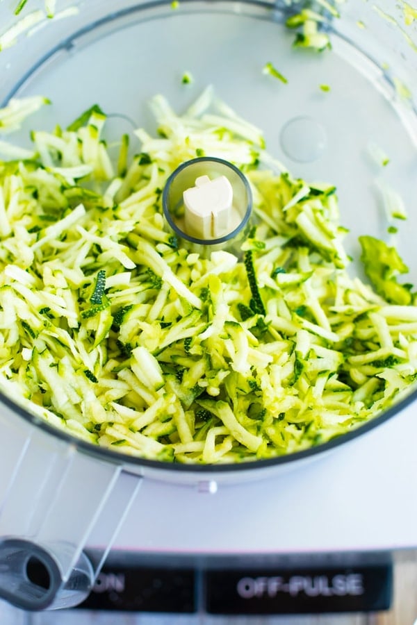 Shredded zucchini inside a food processor to make a zucchini muffin recipe.