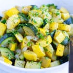 Sautéed zucchini and yellow summer squash in a white bowl with a serving spoon.