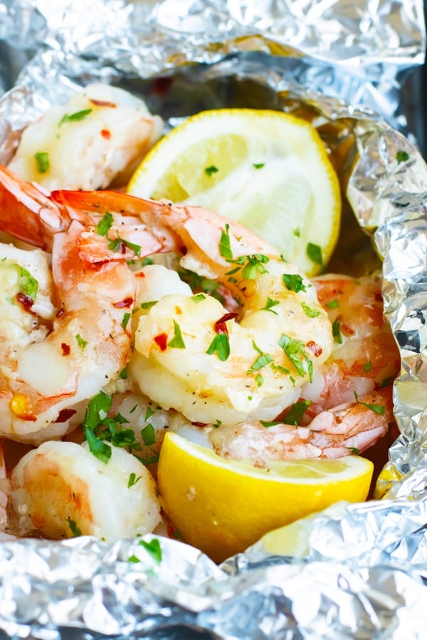 Easy shrimp scampi inside a foil packet with lemon wedges for dinner.