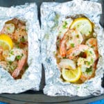 Two baked shrimp foil packets with lemon on a baking sheet.