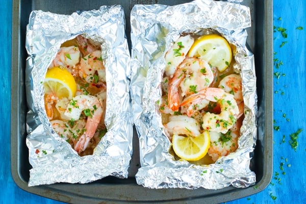 Two baked shrimp foil packets with lemon on a baking sheet.