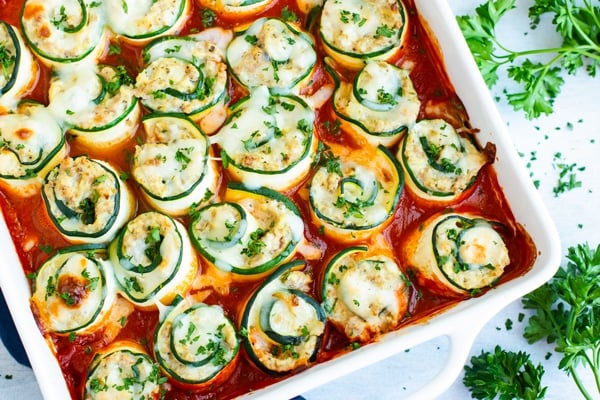 Low carb zucchini lasagna recipe in a white baking dish surrounded by parsley.
