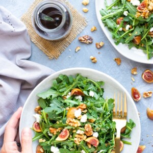 Overhead picture of an Arugula Fig Salad recipe in a bowl with dressing on the side.