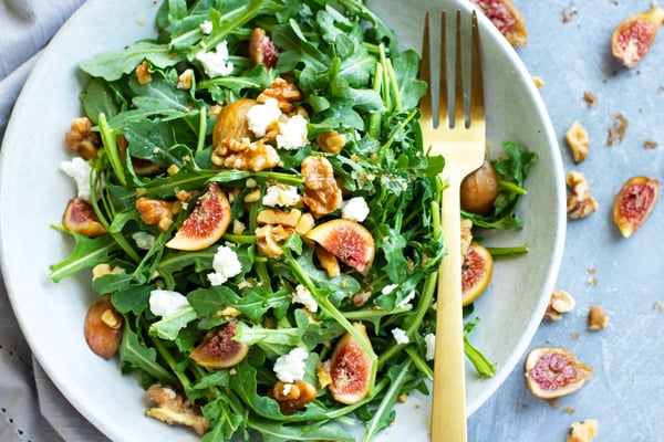 Healthy arugula goat cheese salad in a bowl surrounded by figs.