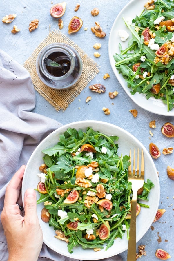 Overhead picture of an Arugula Fig Salad recipe in a bowl with dressing on the side.