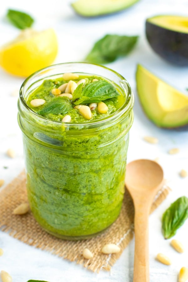 Gluten-free avocado pesto in a glass jar with a wooden spoon on the side.