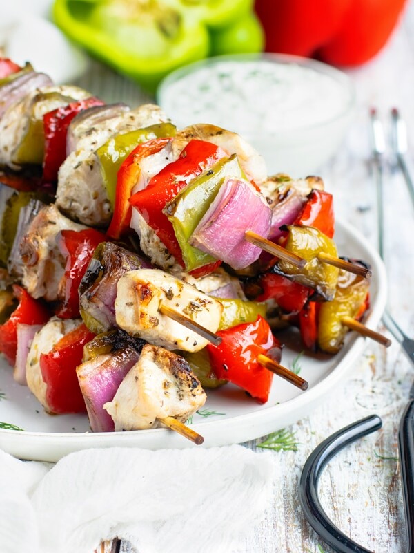 Side picture of a pile of Grilled Greek Chicken Shish Kabobs with sauce in the background.