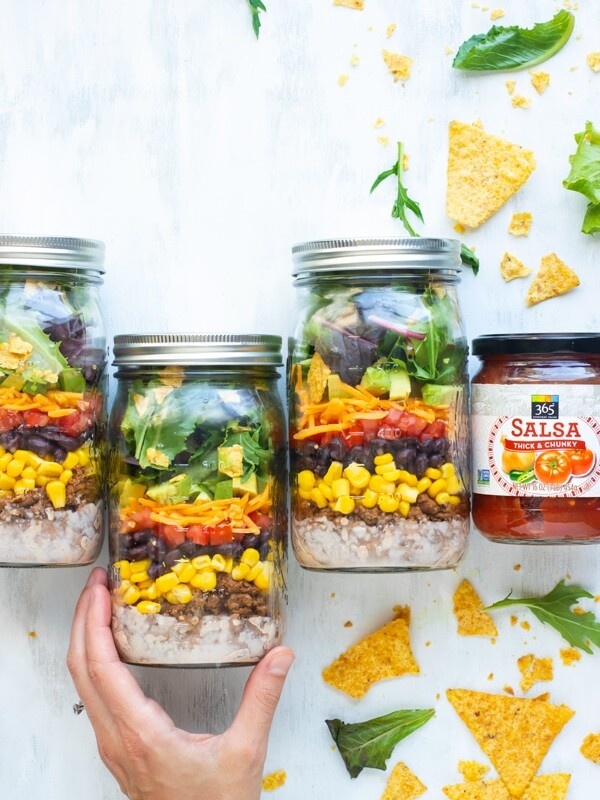 Easy healthy taco salad in mason jars with a jar of salsa on the side.