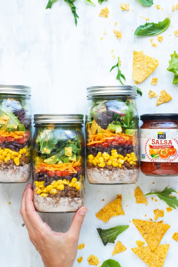 Easy healthy taco salad in mason jars with a jar of salsa on the side.