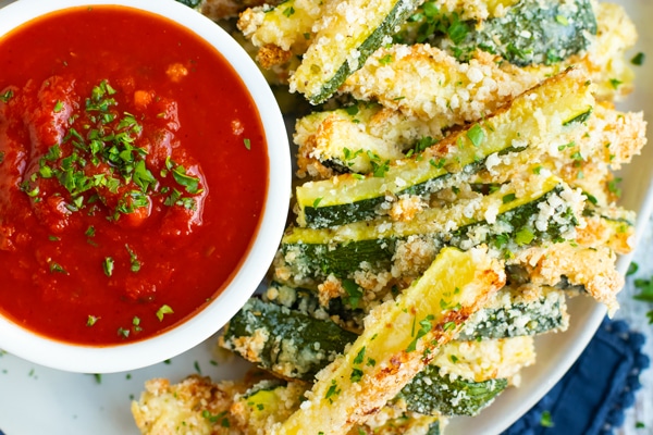Overhead picture of baked parmesan zucchini with sauce on the side.