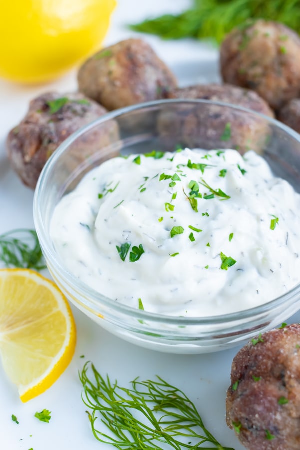 Creamy, authentic Greek tzatziki sauce full of fresh dill and Greek yogurt is placed in a glass bowl for dipping Greek meatballs.