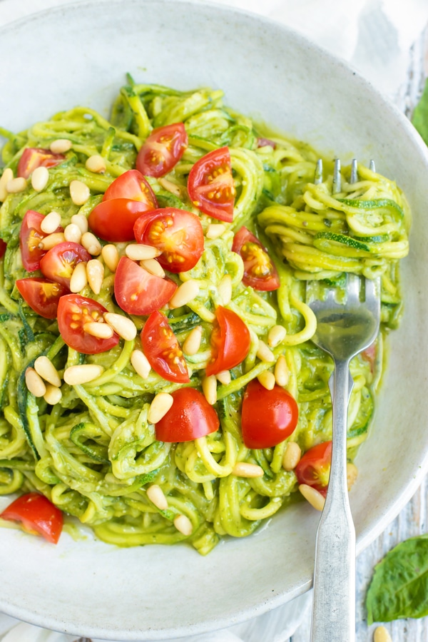 Zucchini noodles with pesto in a bowl with tomato slices for lunch.