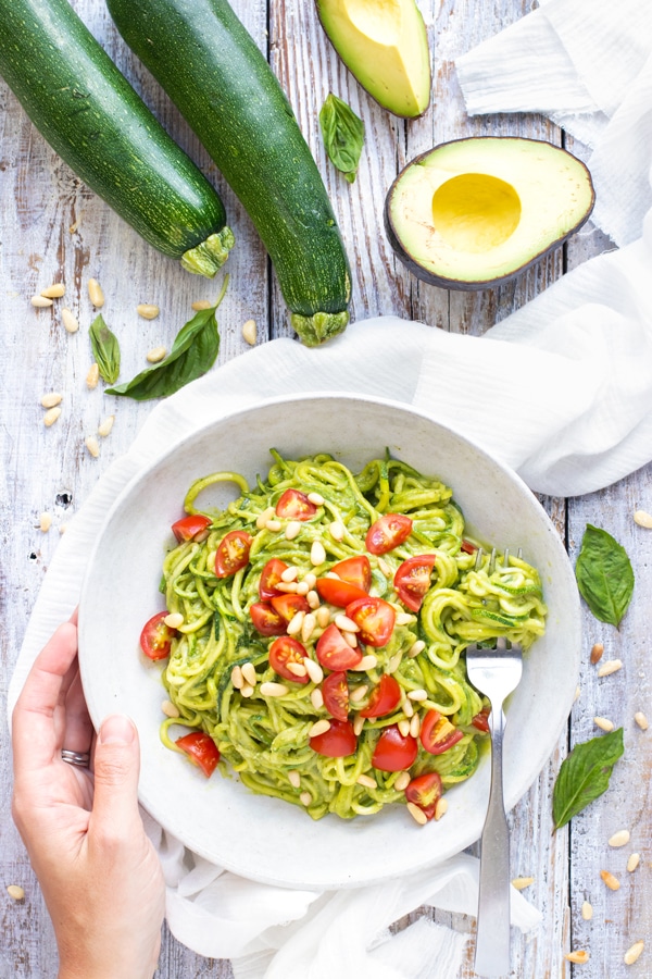 Gluten-free zucchini noodles with pesto in a white bowl with a fork.