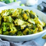 Roasted broccoli recipe in a white bowl with honey on the side.