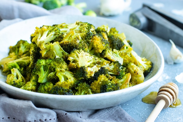 Roasted broccoli recipe in a white bowl with honey on the side.