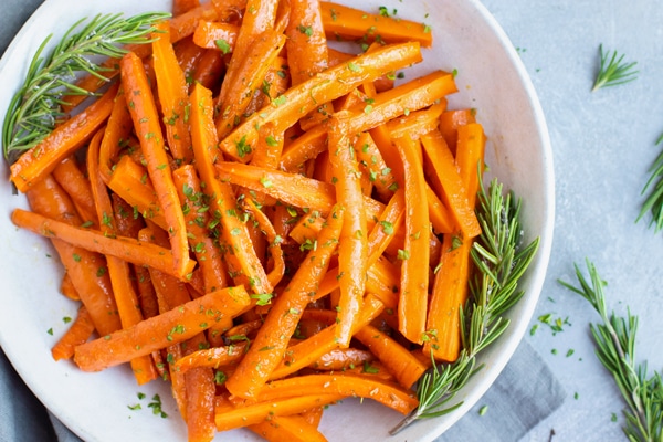 Overhead picture of honey roasted carrots in a white bowl with rosemary.