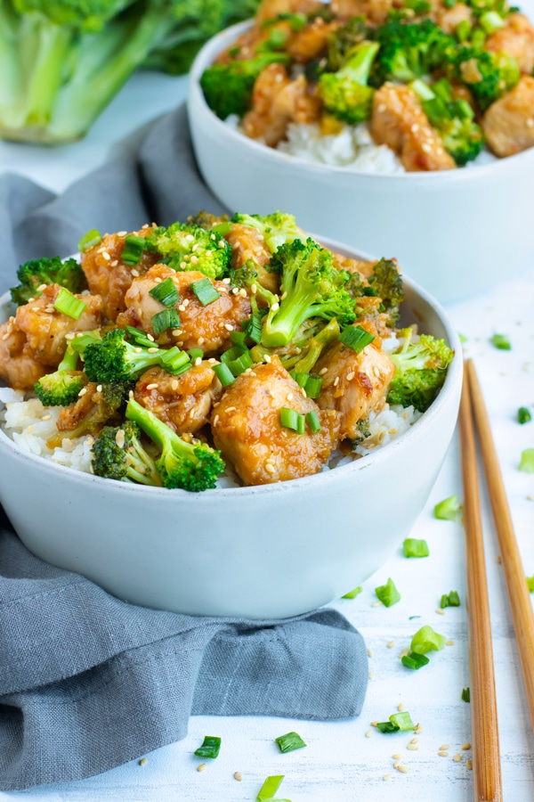 Sesame chicken recipe in a white bowl with rice and chopsticks on the side.