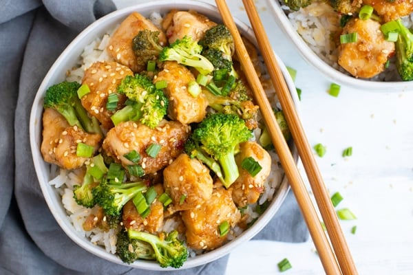 Easy sesame chicken recipe in a white bowl with chopsticks on the side.