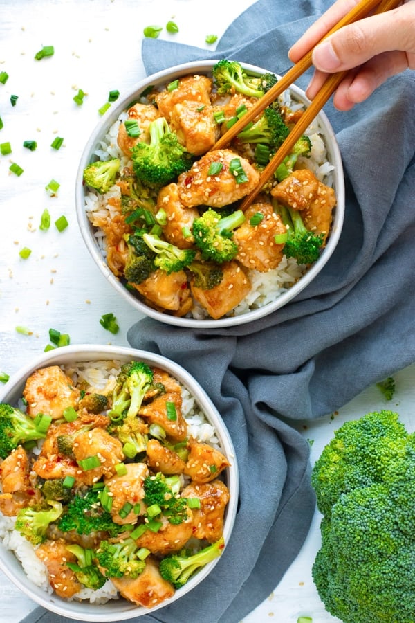 Overhead picture of gluten-free Honey Sesame Chicken in two white bowls with hand held chopsticks.