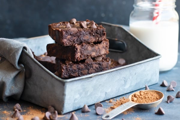 Stack of chocolate chip brownies with a glass of milk in the background.