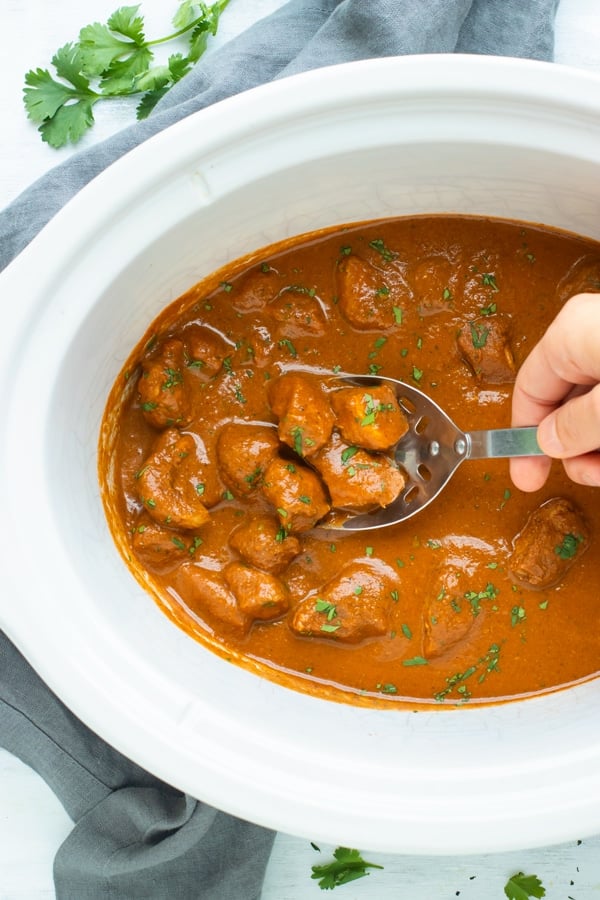 Easy Chicken Tikka Masala in a slow cooker scooped up by a silver spoon.