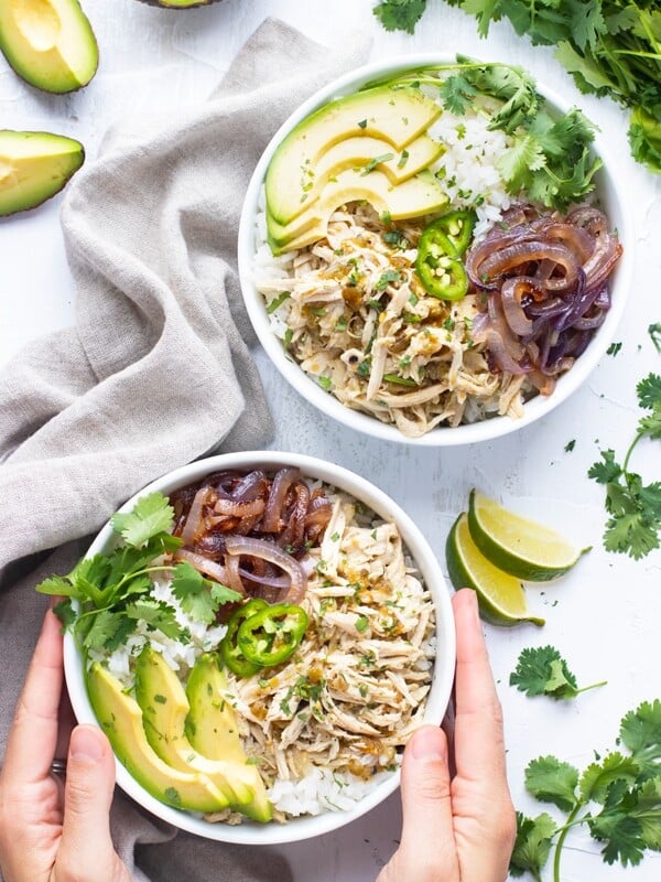 Slow cooker shredded chicken recipe in a white bowl with sliced avocado and other ingredients.