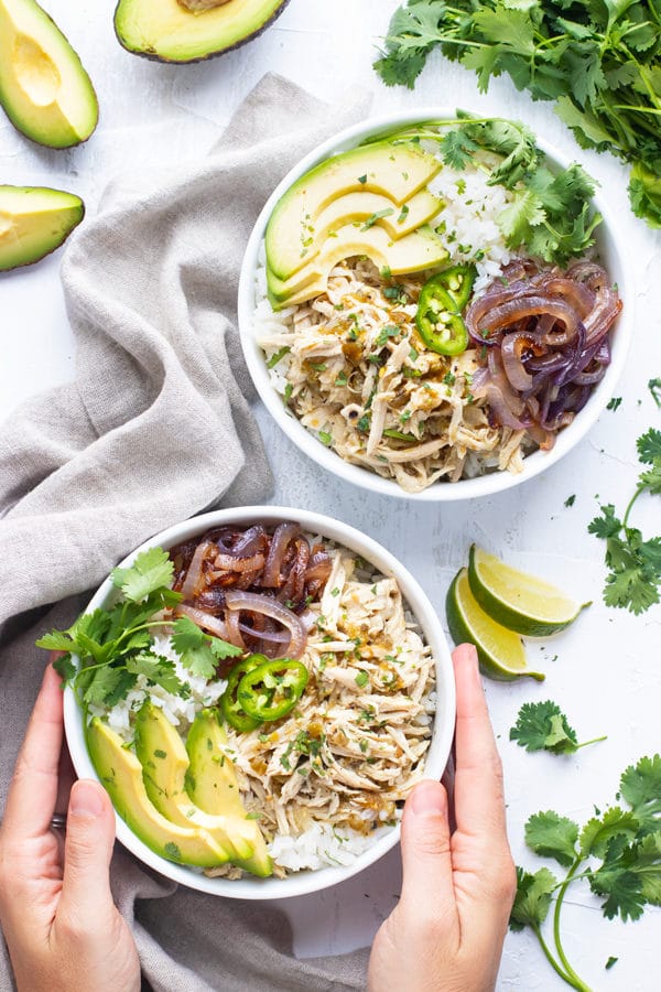 Slow cooker shredded chicken recipe in a white bowl with sliced avocado and other ingredients.