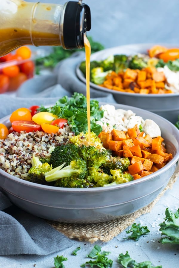 Salad dressing being poured into a quinoa bowl recipe.