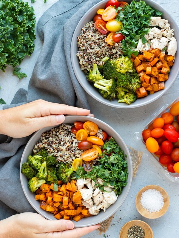 Two hands holding a gray bowl filled with a veggie quinoa bowl recipe.
