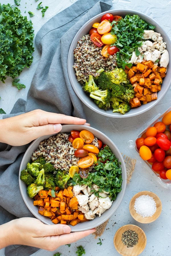 Two hands holding a gray bowl filled with a veggie quinoa bowl recipe.