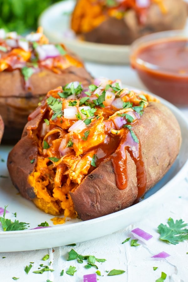 BBQ Chicken Stuffed Sweet Potato that is on a white plate and sprinkled with cilantro and red onions.