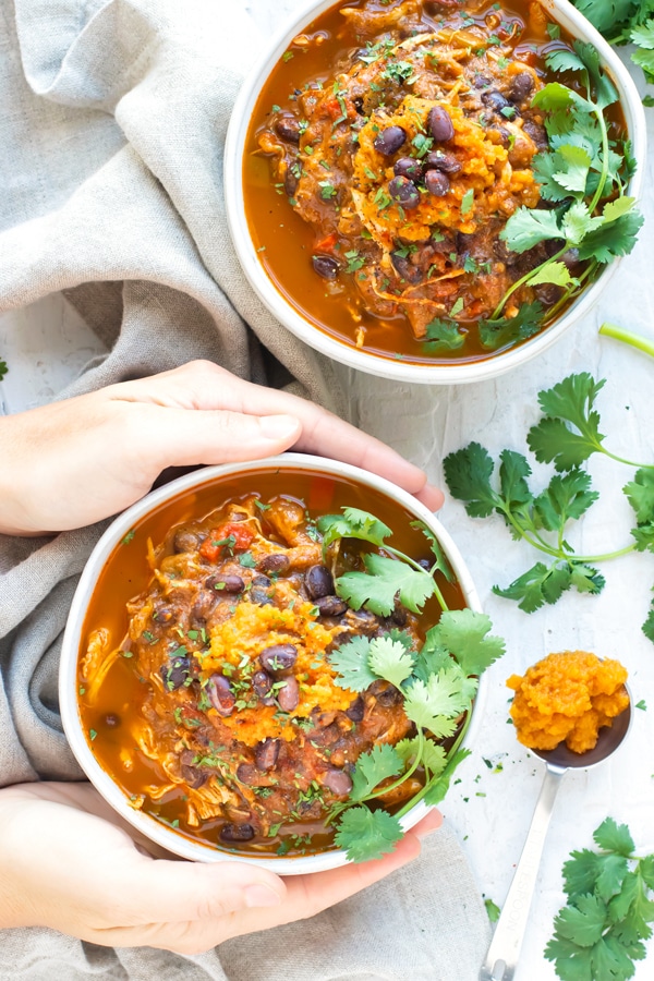 Instant Pot Pumpkin Chicken Chili in white bowls with hands holding it.