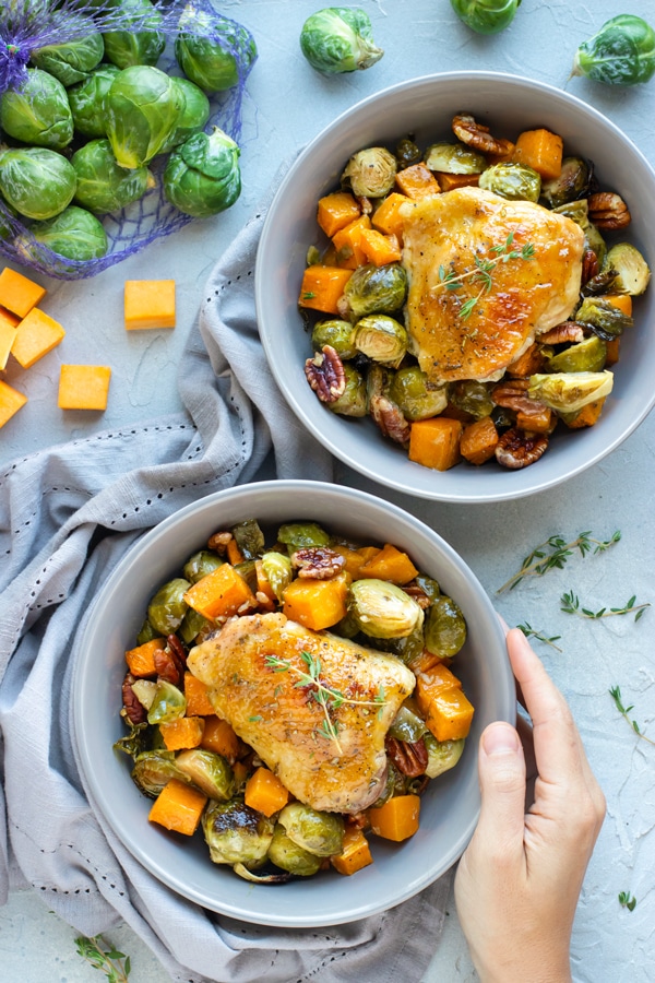 Hand touching Maple Dijon Chicken and veggies in two bowls.