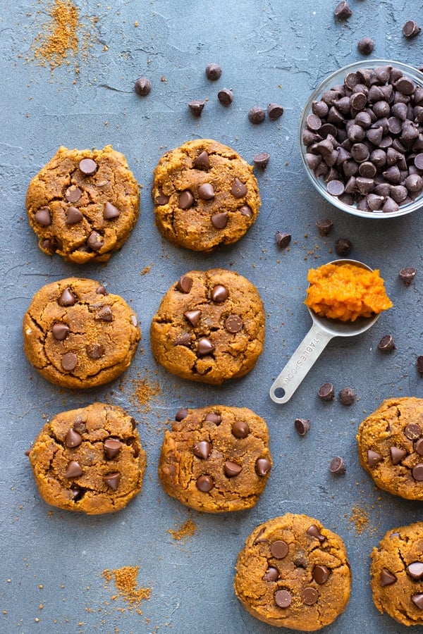 Pumpkin Chocolate Chip Cookies Recipe on a grey backdrop with chocolate chips and pumpkin puree.