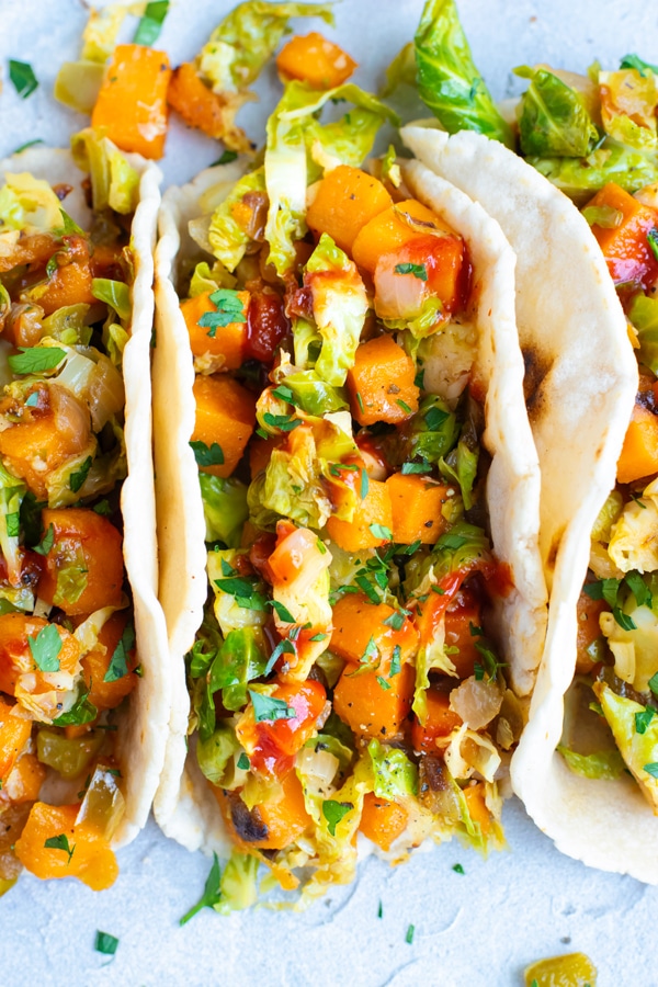 Vegan tacos filled with sweet potatoes and Brussel sprouts on a white table.