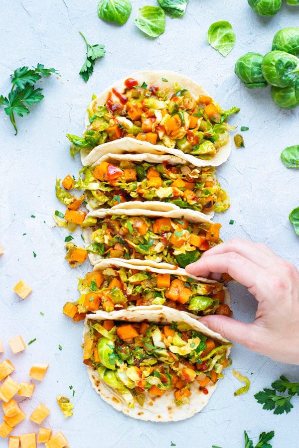 Overhead shot of a hand touching a row of vegan tacos.