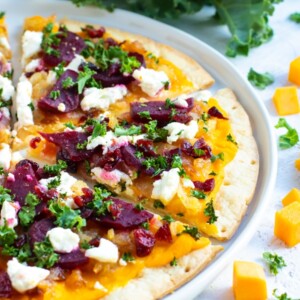 Butternut Squash Pizza is made from a gluten-free pizza crust, covered in a creamy butternut squash pasta sauce, and then topped with beets, caramelized onions, kale, and dried cranberries!  This gluten-free pizza recipe can easily be made vegan and will change up the way you think about your favorite pie!