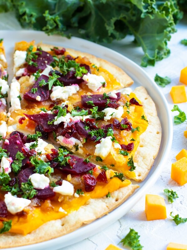 Butternut Squash Pizza is made from a gluten-free pizza crust, covered in a creamy butternut squash pasta sauce, and then topped with beets, caramelized onions, kale, and dried cranberries!  This gluten-free pizza recipe can easily be made vegan and will change up the way you think about your favorite pie!