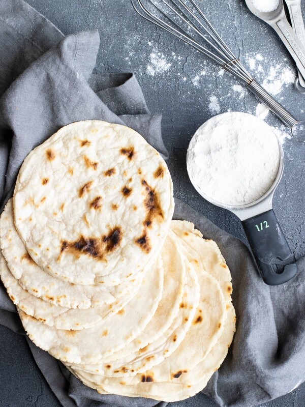 Paleo tortillas on a gray napkin with a half-cup of flour next to them.