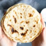 A pair of hands holding a stack of tortillas that are made with a delicious paleo tortilla recipe.