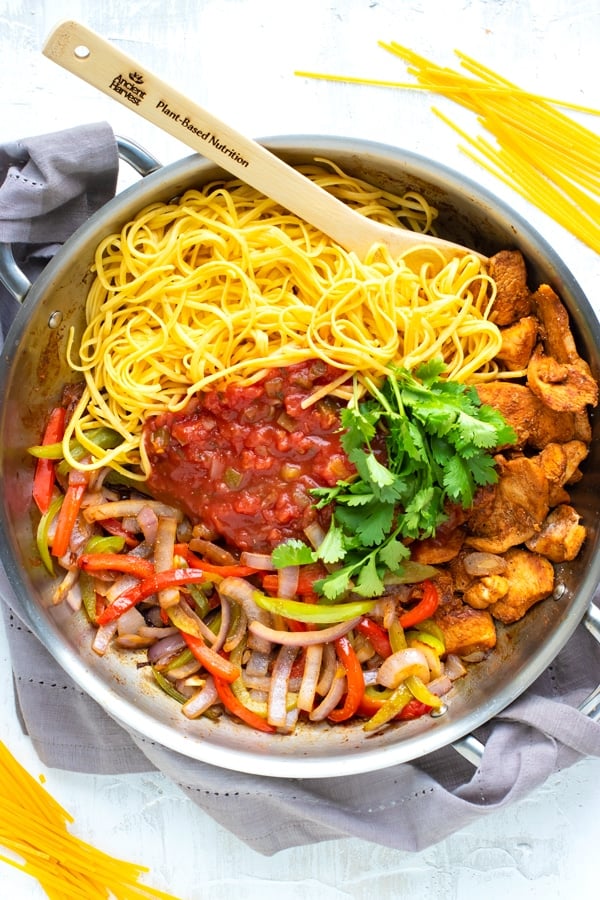 Gluten free pasta, chicken fajita meat, bell peppers, onions, salsa, and cilantro in a skillet to make chicken fajita pasta.