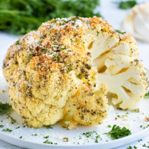 Part of a whole roasted cauliflower seasoned with herbs on a white plate.