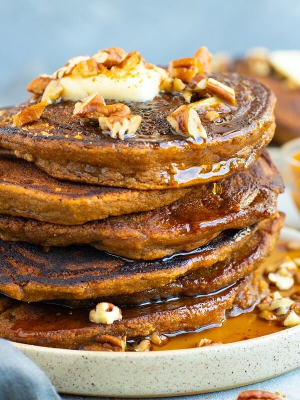 Pumpkin pancakes in a stack with pecans and maple syrup.