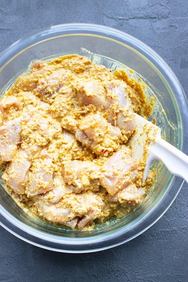 Korma sauce and chicken thighs in a clear bowl with a white spoon stirring it.