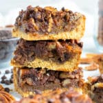 An easy pecan pie bars recipe in a stack with chocolate chips on a white background.