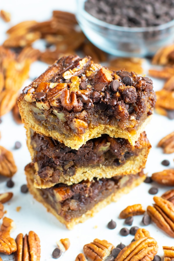 A stack of pecan pie bars with chocolate chips and pecans surrounding them.