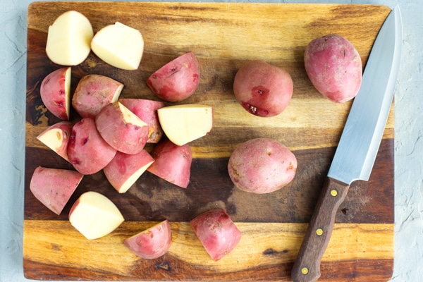Cut red skin potatoes on a cutting board with a knife for red skin mashed potatoes recipe.