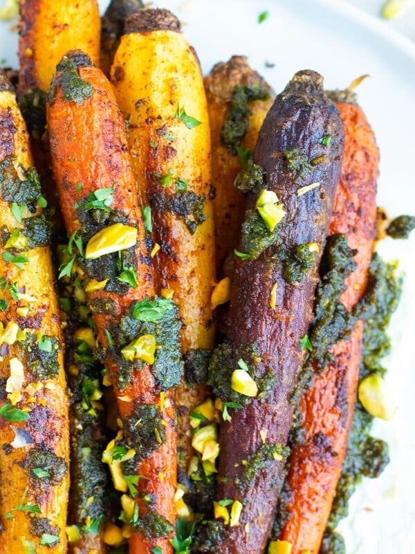 Roasted rainbow carrots with pistachio pesto and a sprinkle of pistachios on a white plate.
